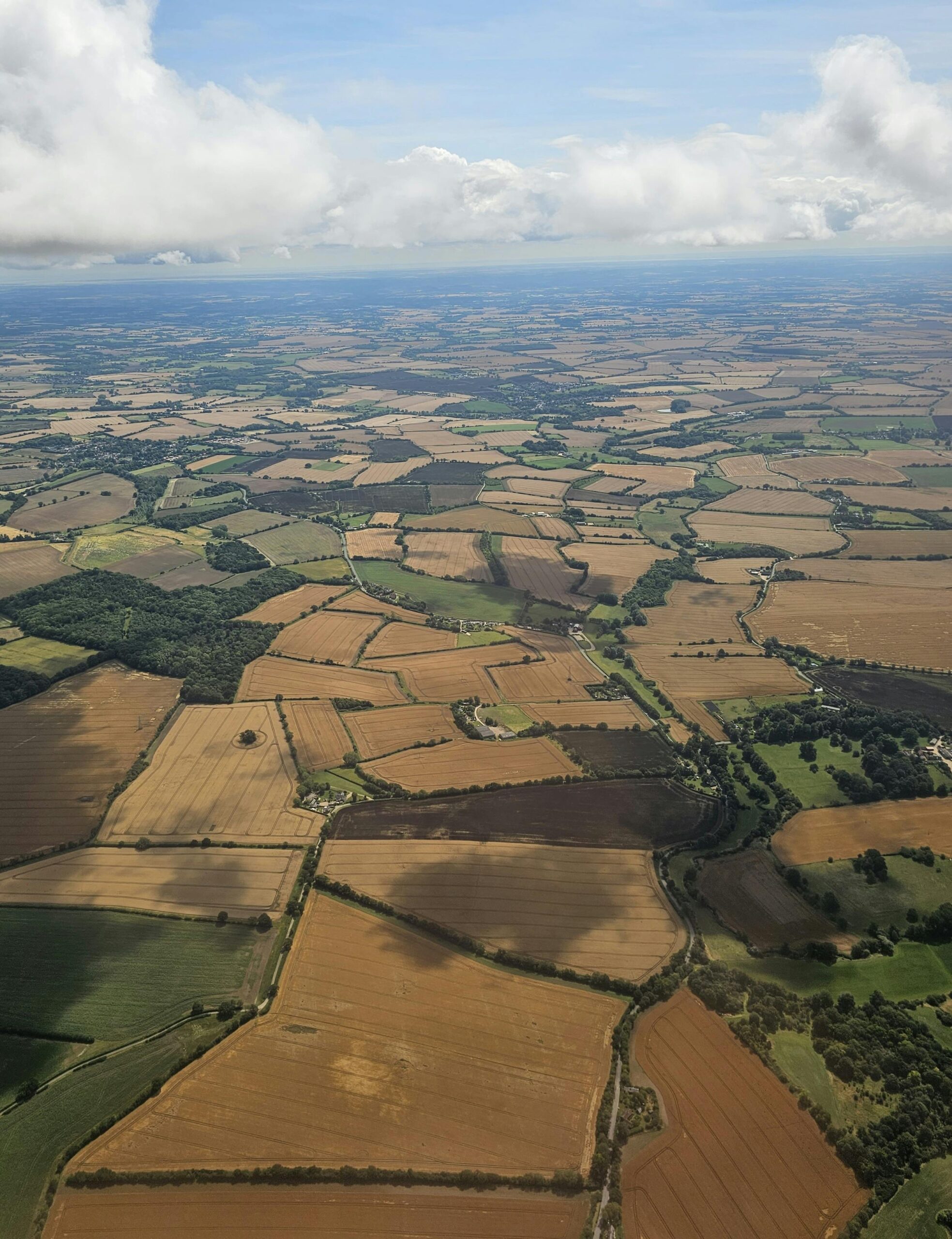 Wide aerial view of patterned farmland stretching to the horizon under a cloudy sky.